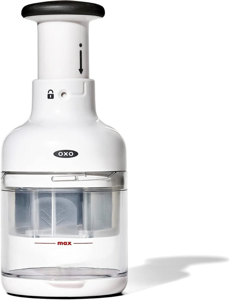 White vegetable chopper with a black push handle and a clear catch container marked with a “max” fill line; OXO logo on the front and a lock icon near the top